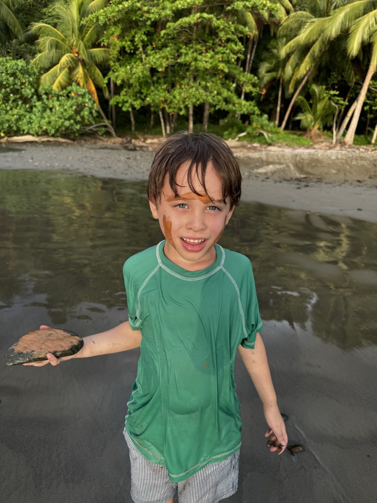 A six-year-old boy at Playa Ventanas holding a flat stone he ground down to make orange paint for his face